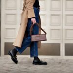oman walking street in fashionable spring or autumn clothes cashmere coat, jeans, black loafers shoes and handbag. Female model in motion, street style fashion, close up legs