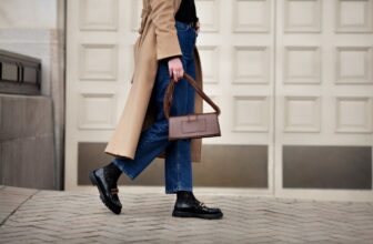 oman walking street in fashionable spring or autumn clothes cashmere coat, jeans, black loafers shoes and handbag. Female model in motion, street style fashion, close up legs