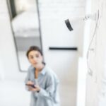 Woman controls home video surveillance with a smartphone indoors, view from the above and ip camera on the foreground. Concept of a wireless home security systems