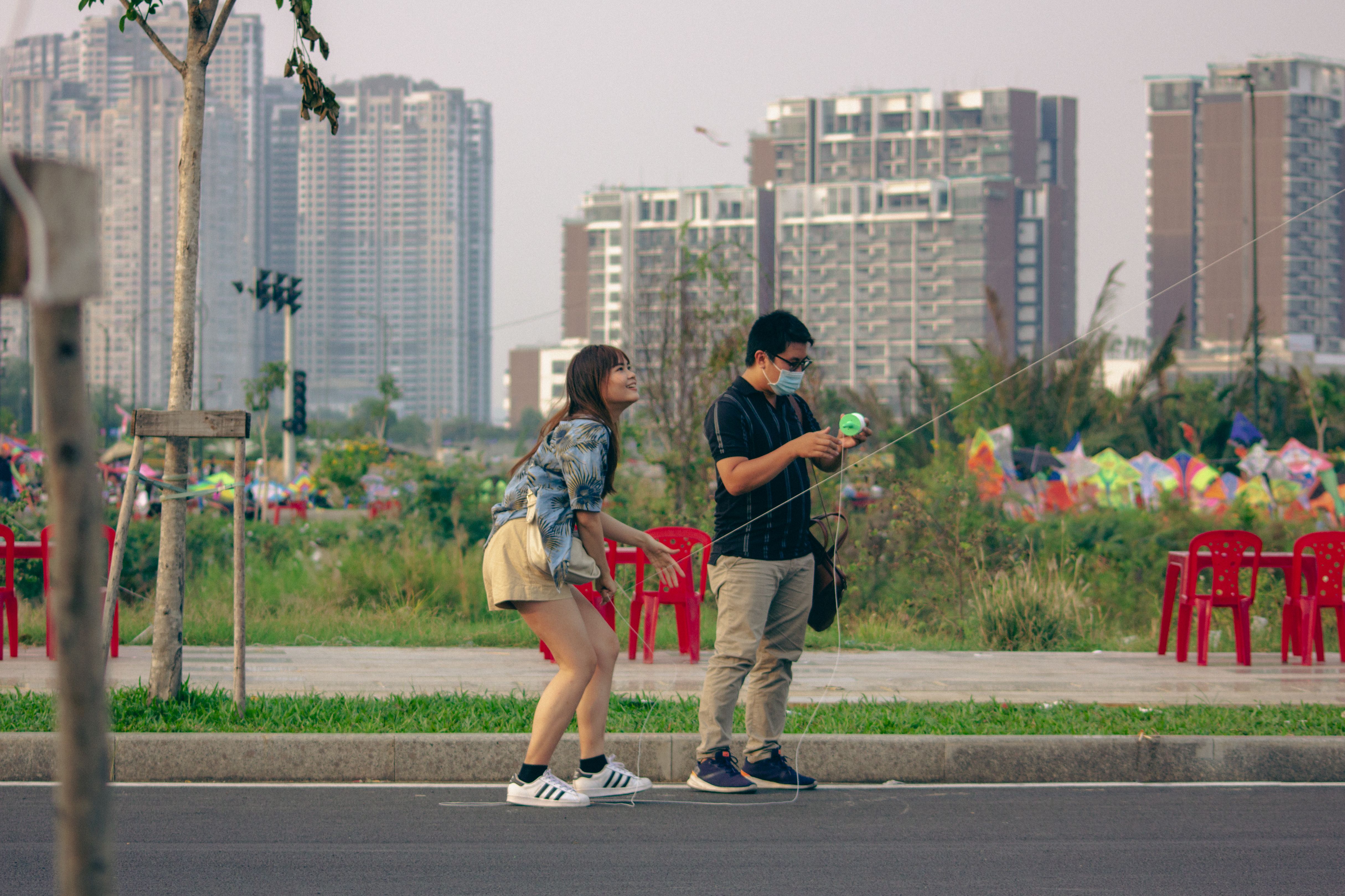 A couple flies a kite together in a city park, embracing childlike play