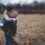 A happy couple shares a playful moment in a sunny field, laughing and embracing