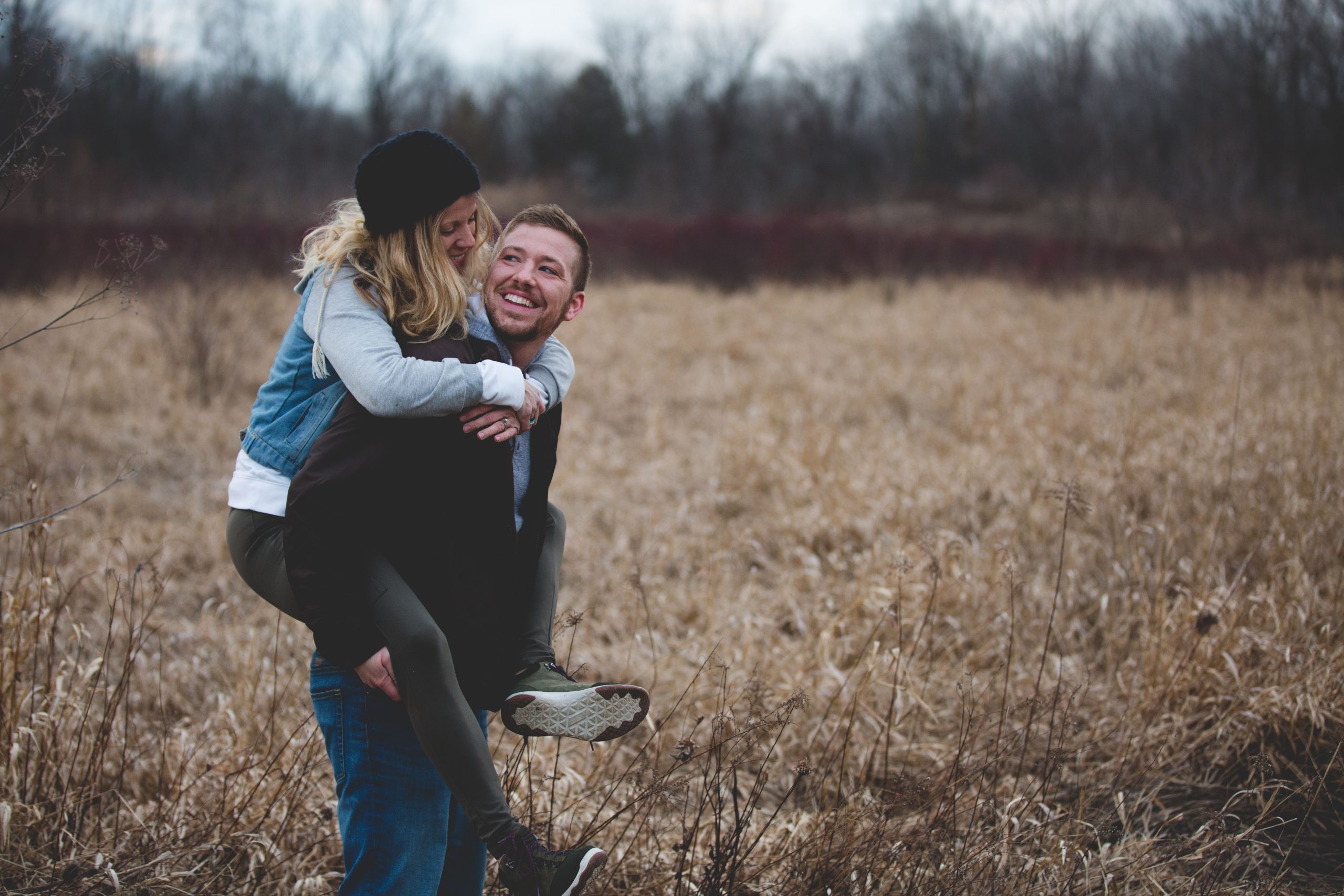 A happy couple shares a playful moment in a sunny field, laughing and embracing