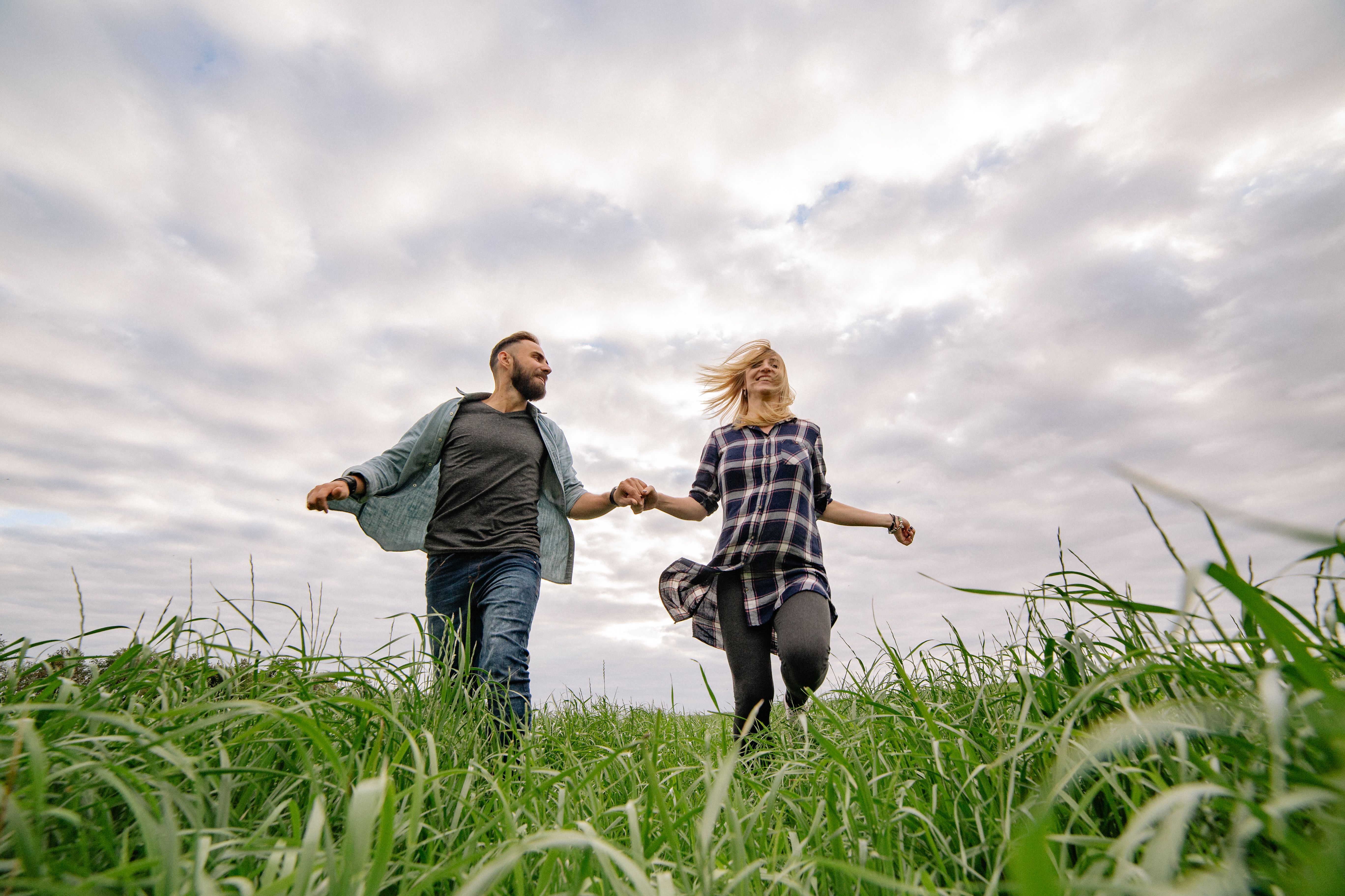 A couple runs hand in hand through a green field, savoring the excitement of shared adventure