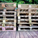 Stacked wooden pallets beside a green outdoor deck, illustrating reclaimed wood reuse for outdoor projects.