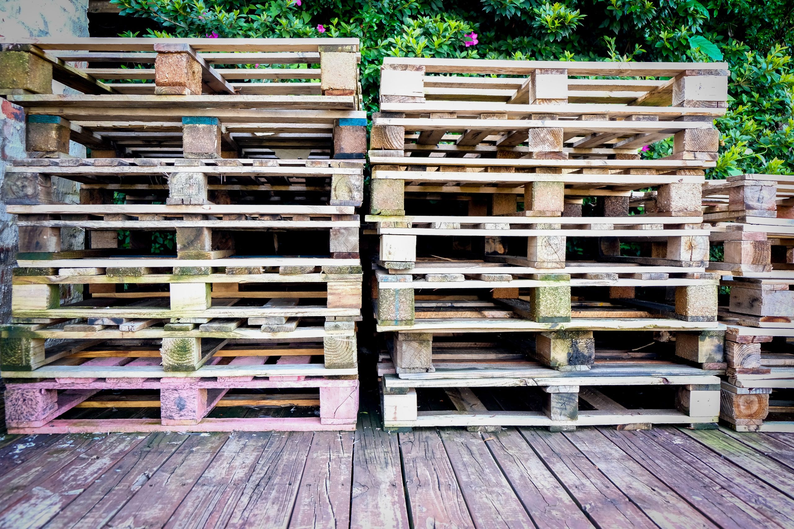 Stacked wooden pallets beside a green outdoor deck, illustrating reclaimed wood reuse for outdoor projects.