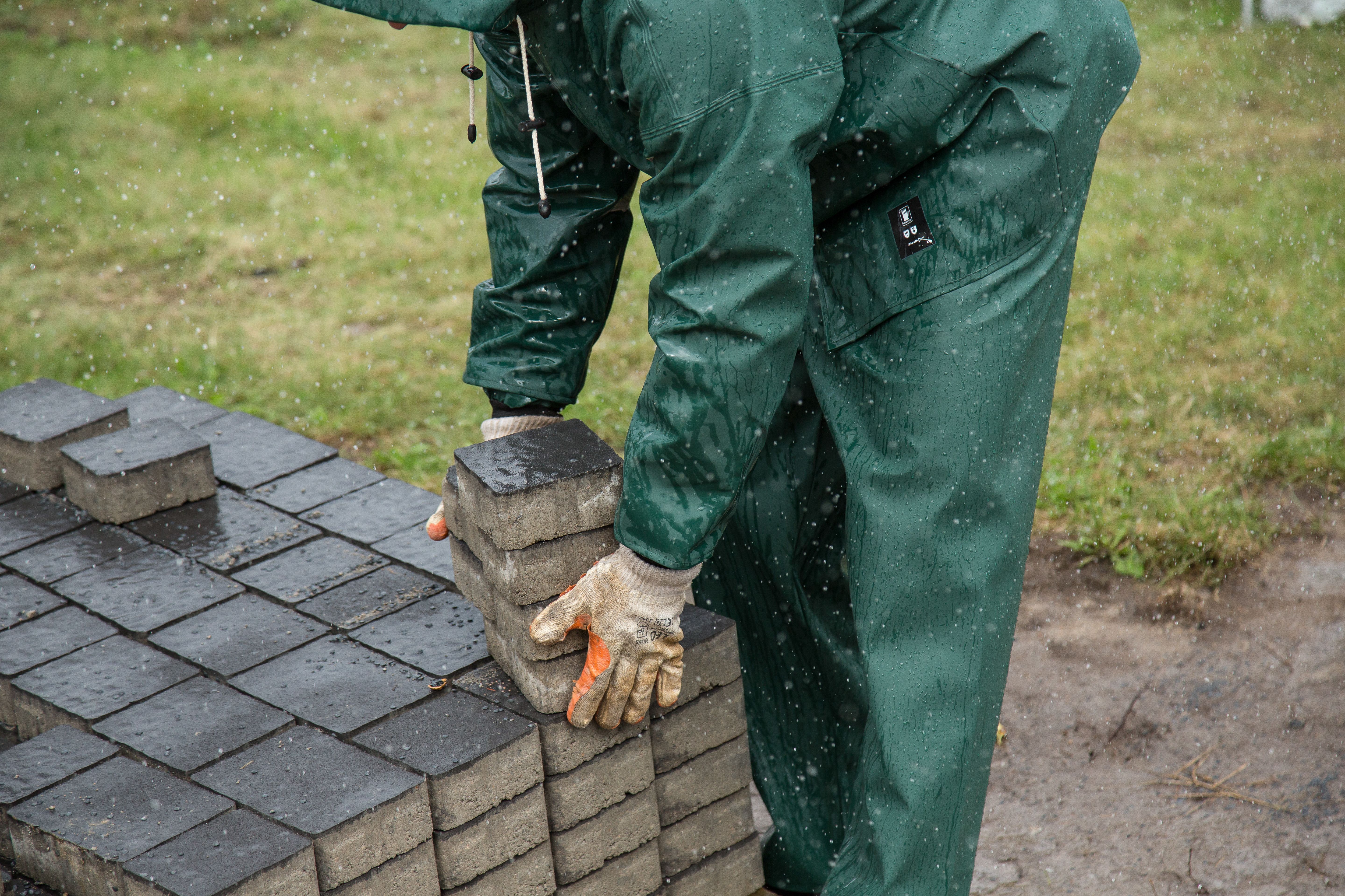 Worker placing paving stones during an outdoor construction project, illustrating hardscape installation.